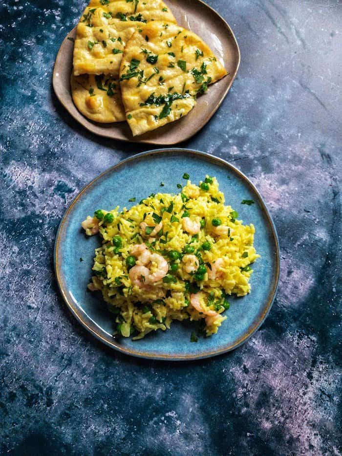 Plate of prawn pilaf next to a plate with buttered flatbread.