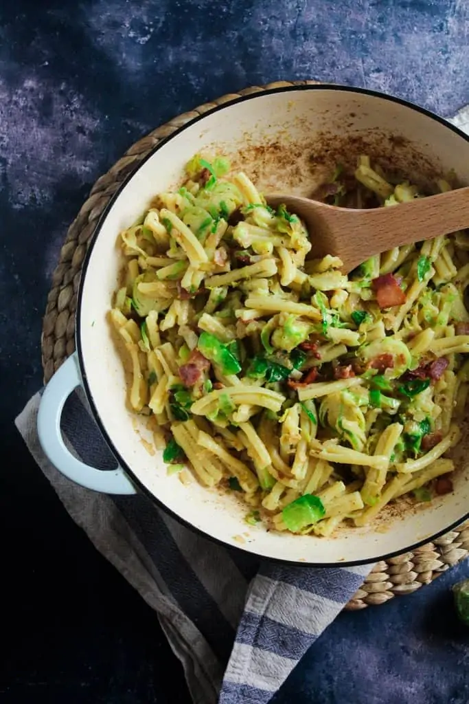 Pasta mixed with bacon, brussels sprouts and a carbonara style sauce in a blue casserole dish. 