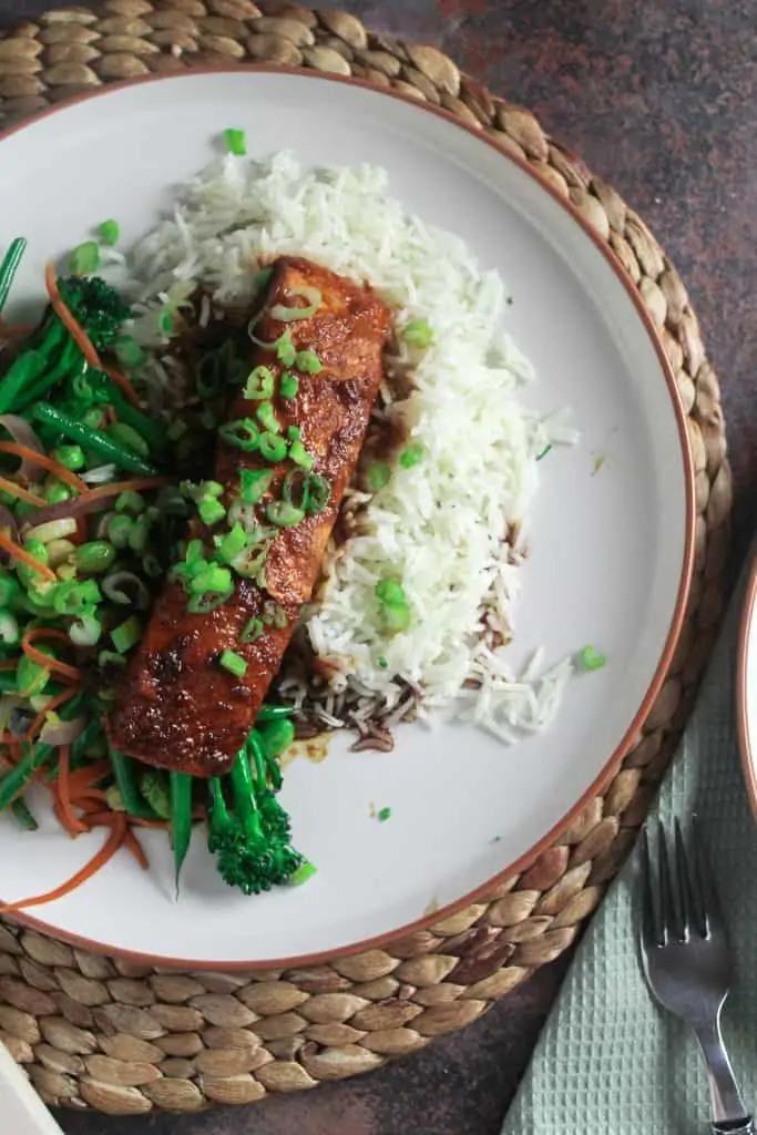 Salmon with a soy and sweet chilli sauce, on a bed of white rice with a side of stir fried green vegetables.