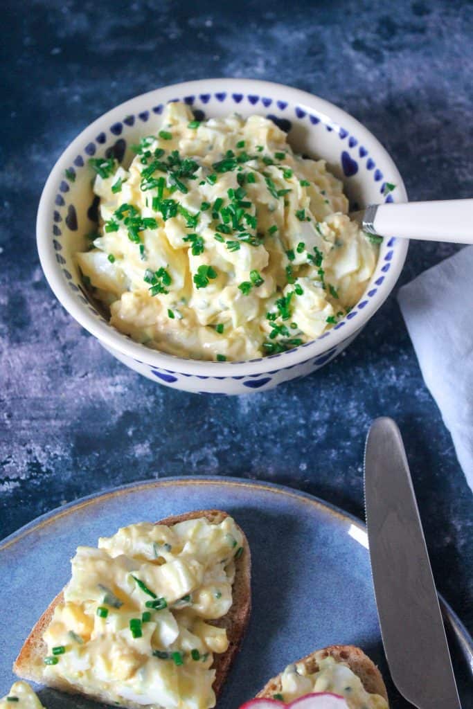 close up of a bowl of egg salad garnished with chopped chives 