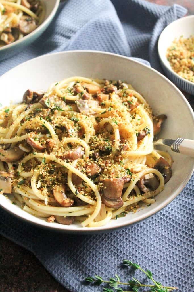 Close up of spaghetti with garlic mushrooms, topped with breadcrumbs.