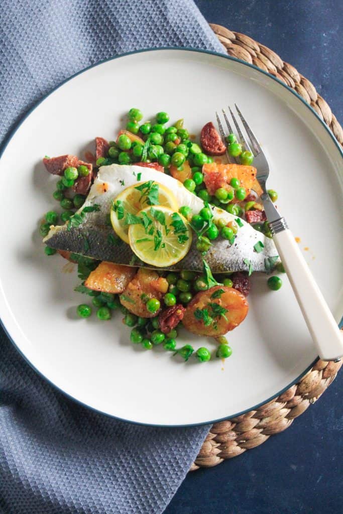 Skin-on sea bass fillet garnished with lemon slices. Served on a bed of green peas, sliced baby potatoes and chunks of chorizo sausage. 