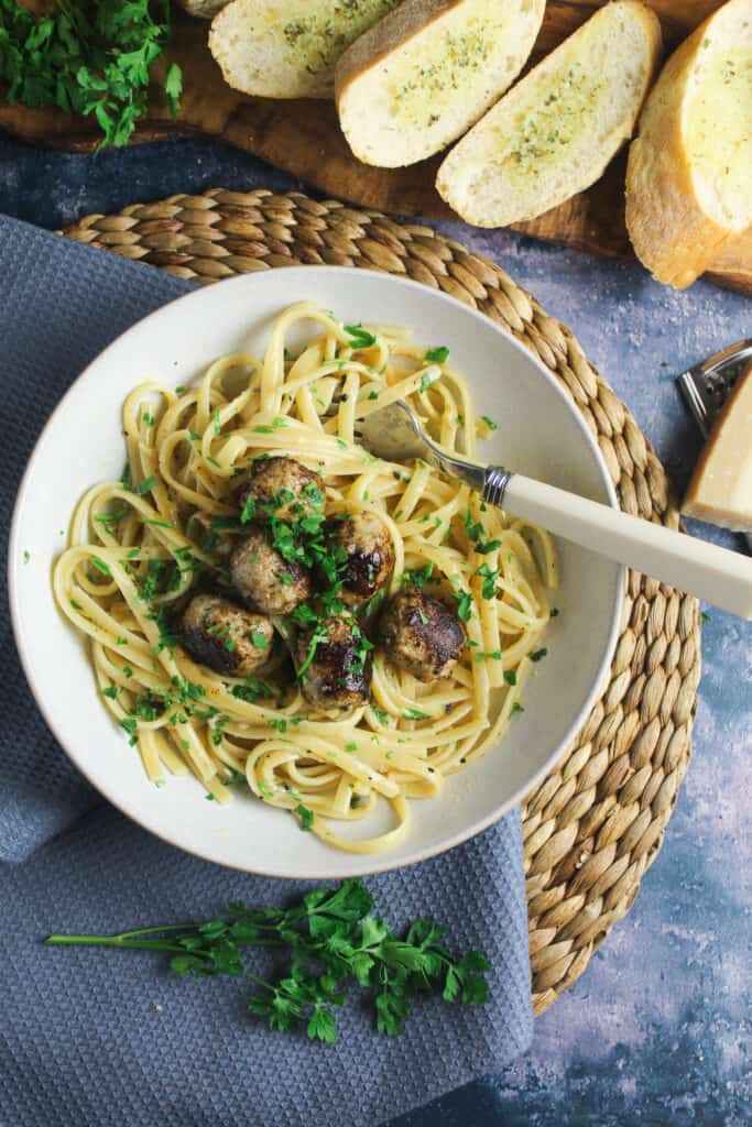 White bowl on a woven mat containing spaghetti topped with sausage meatballs and sprinkled with parsley. 