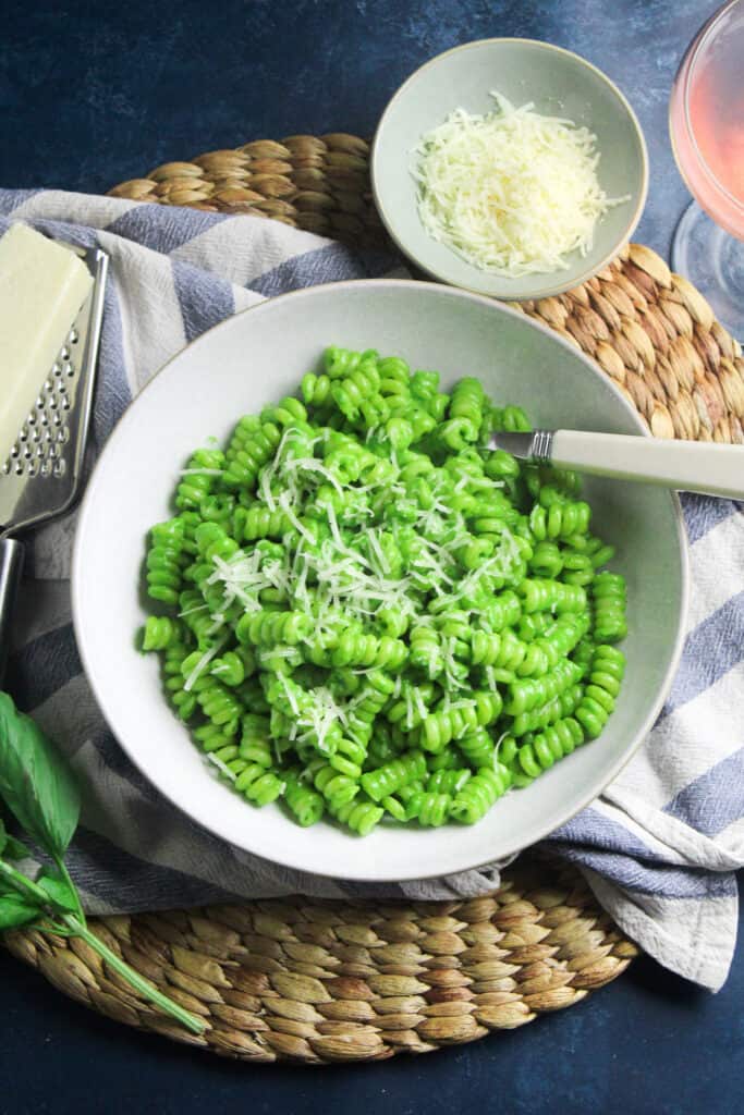 White bowl containing pasta spirals in a bright green spinach sauce, topped with grated parmesan. 