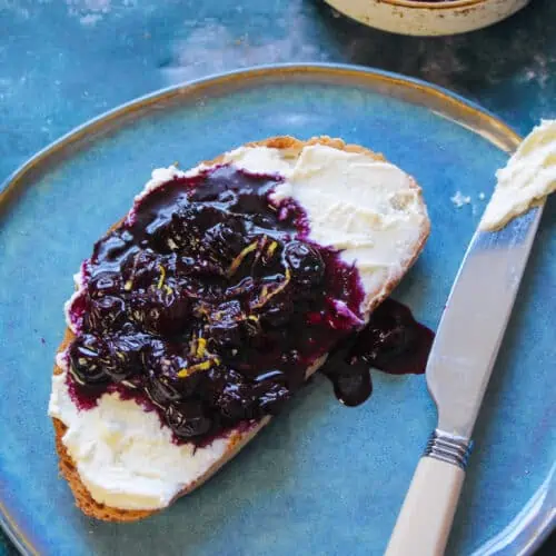 Toast slice spread with ricotta cheese and a spoonful of blueberry sauce.