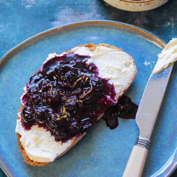 Toast slice spread with ricotta cheese and a spoonful of blueberry sauce.