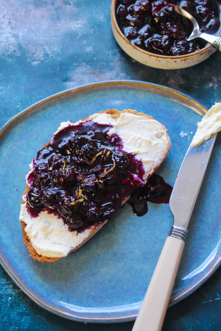 Toast slice spread with ricotta cheese and a spoonful of blueberry sauce.