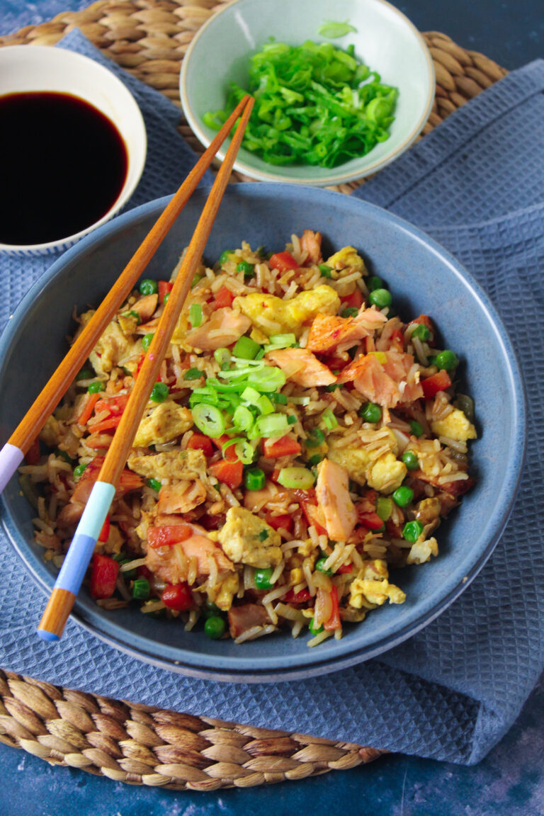Blue bowl containing salmon and egg fried rice with peas and carrots.