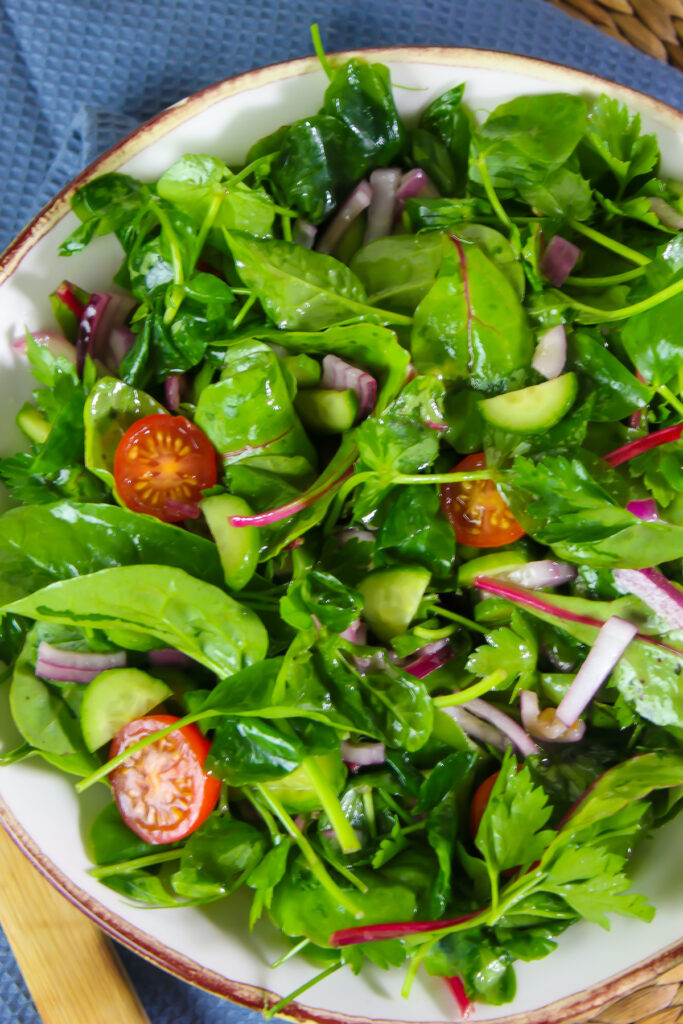 Green salad leaves tossed with lemon juice and olive oil in a large white salad bowl.