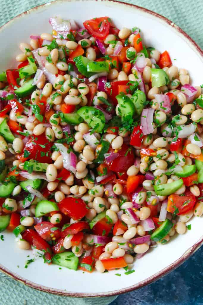 Large white bowl containing white bean salad with tomato, onion and cucumber.