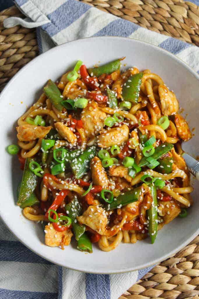 Chilli Garlic Chicken Noodles with red pepper, sugar snap peas and scallions in a white bowl. 