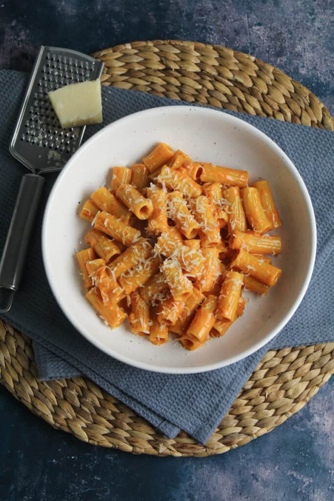 Gochujang Vodka Rigatoni sprinkled with grated parmesan cheese in a white pasta bowl placed on a blue table linen. 