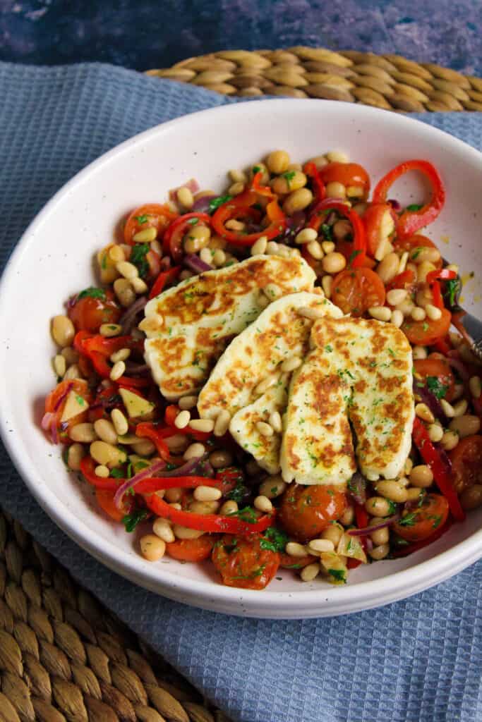 Slices of fried halloumi cheese on a salad of haricot beans, sliced pepper, red onion and cherry tomatoes. 