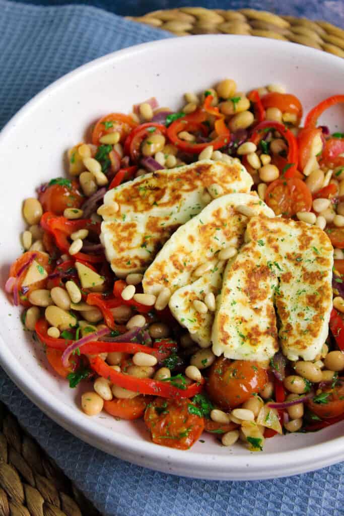 Close up of halloumi slices served on tomato and white bean salad. 