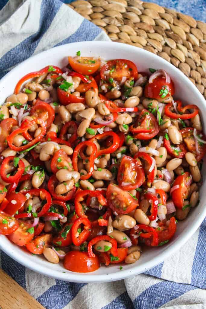 White bowl containing borlotti beans, sliced cherry tomatoes and red pepper tossed with parsley and a sherry vinaigrette. 