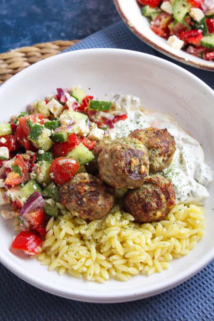 Air fryer turkey and feta meatballs on a bed of cooked orzo pasta with a side of cucumber salad and tzatziki dip.