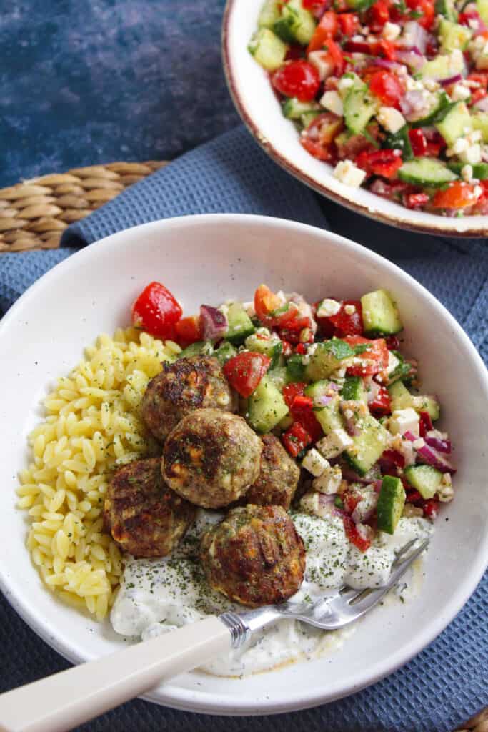 White bowl with orzo pasta, Greek style salad and turkey meatballs.