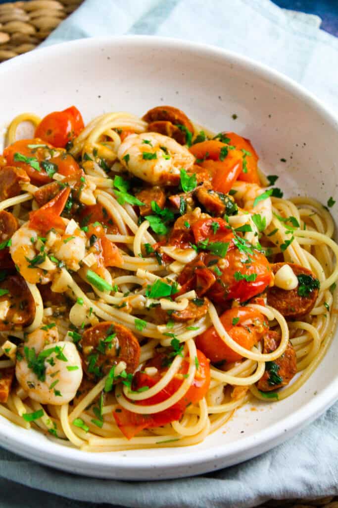 Spaghetti with jumbo shrimp, sliced chorizo and cherry tomatoes garnish with chopped parsley. 