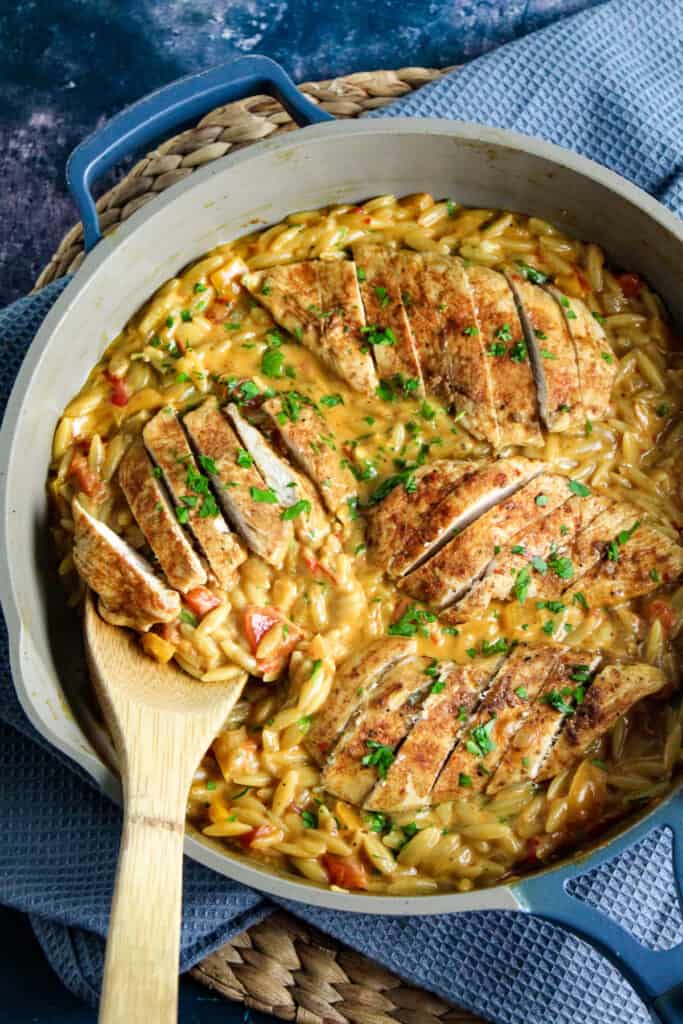 A skillet containing orzo in a creamy cajun sauce topped with sliced chicken breast. 