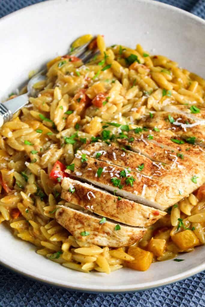 Sliced chicken breast on top of orzo pasta in a cajun cream sauce with diced pepper and tomato. 