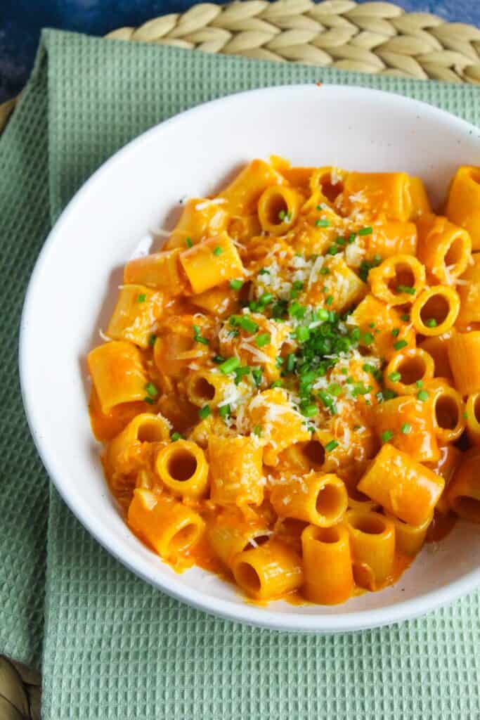 Rigatoni pasta in a creamy red gochujang sauce garnished with chopped chives and grated cheese.