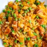 A plate of pasta with peas, chicken and chorizo chunks.