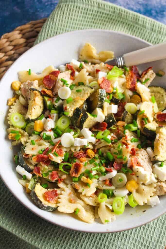 A bowl of pasta with chicken, zucchini and green onions.