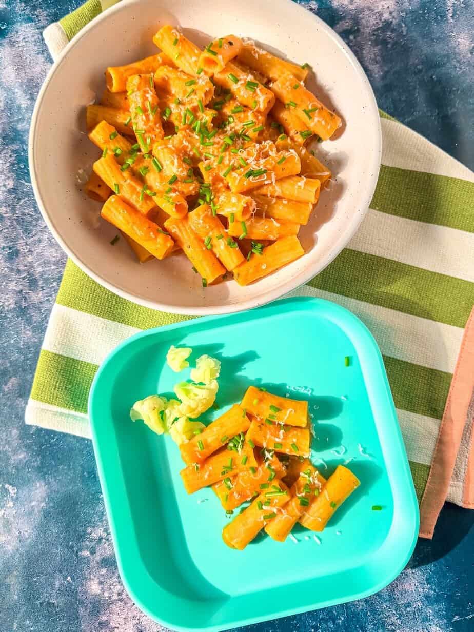 A child plate and adult plate of pasta with cheese and vegetables.