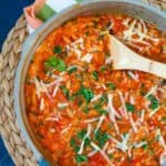 A pan of tomato and orzo pasta with a wooden spoon.