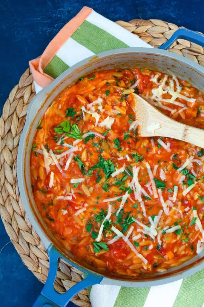A pan of tomato and orzo pasta with a wooden spoon.