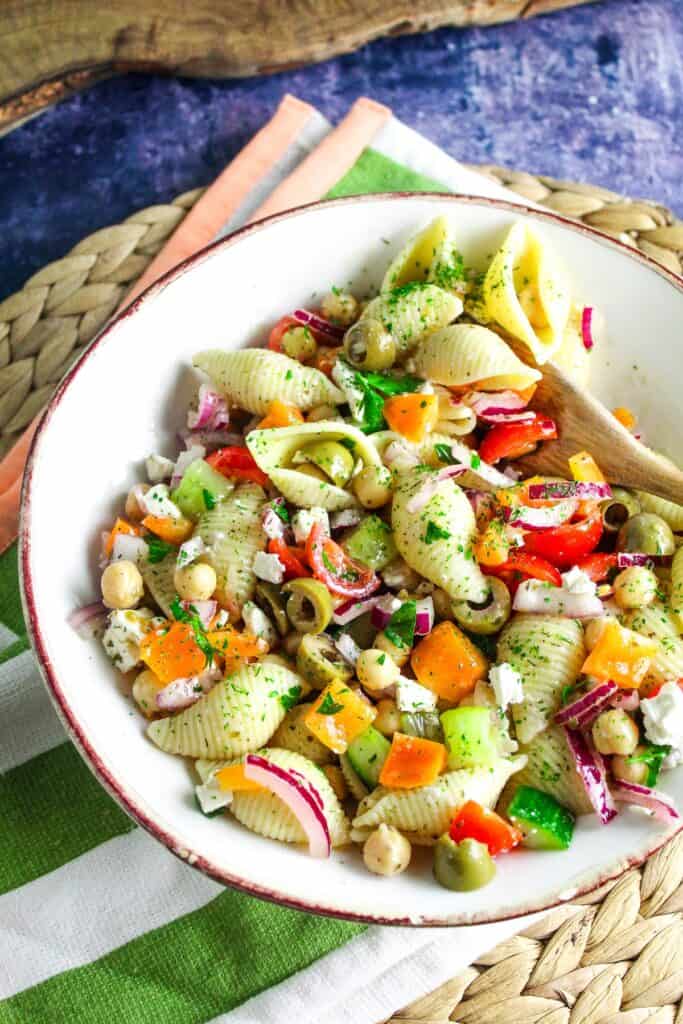 A bowl of pasta salad with cucumbers, peppers and olives.