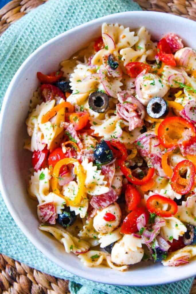 Colorful pasta salad with cherry tomatoes, olives, and fresh herbs in a white bowl.