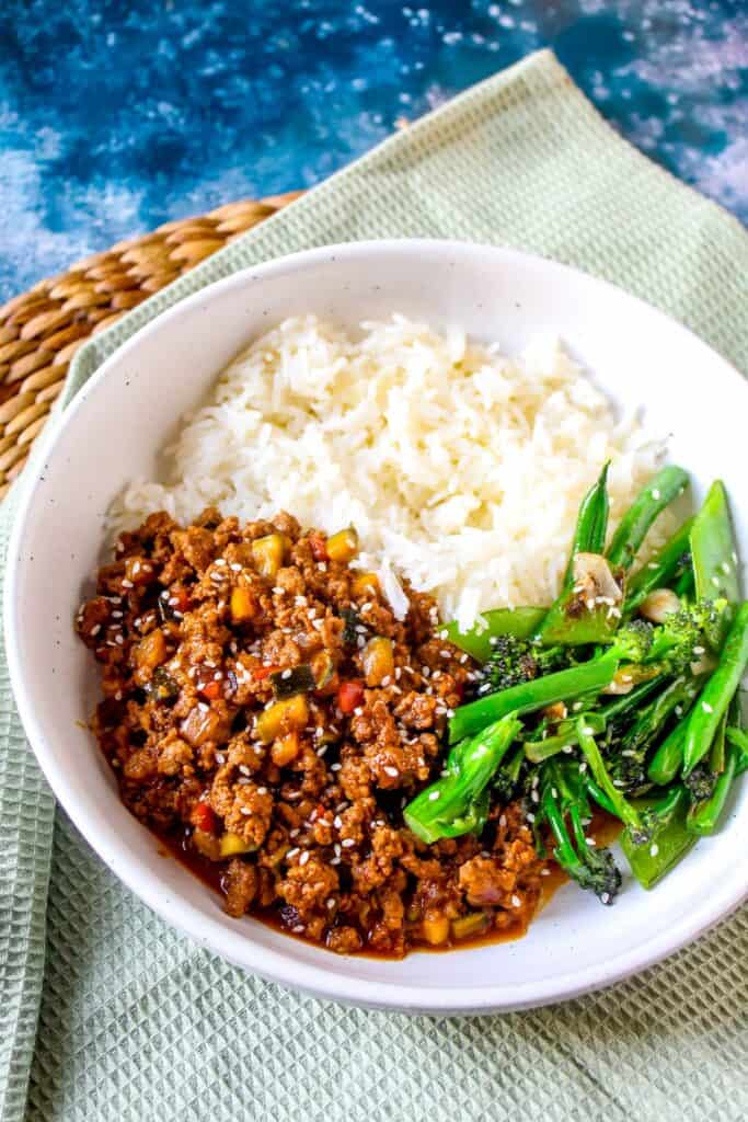 Savory ground beef and vegetable stir-fry with rice and greens in a white bowl.