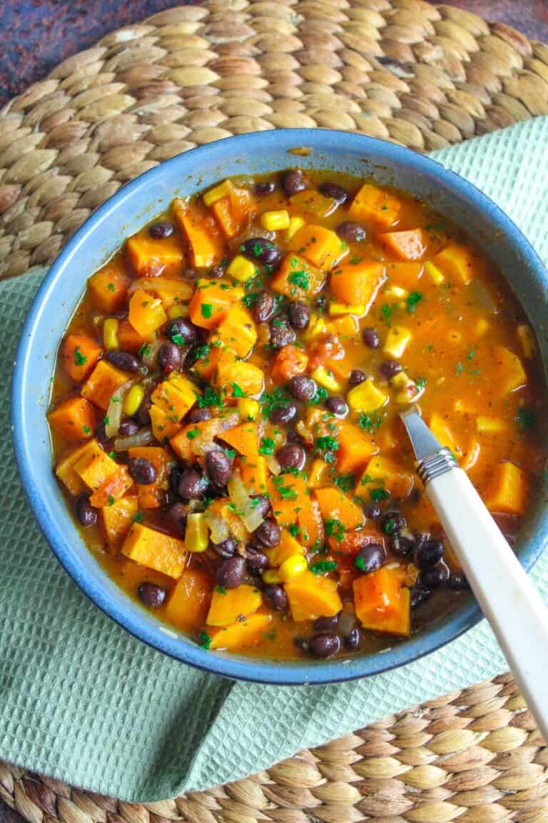 Sweet potato black bean soup with corn and herbs in a blue bowl on a woven placemat.