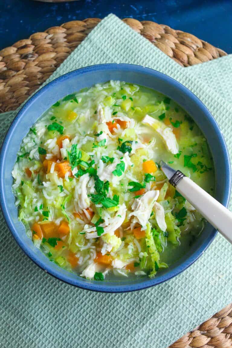 Chicken and leek soup with fresh herbs and rice in a blue bowl.