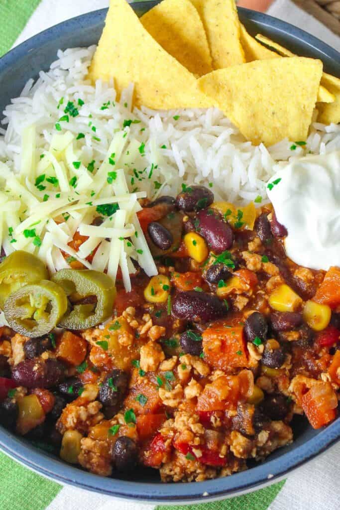 Turkey chili with black beans, corn, cheese, sour cream, and tortilla chips on a blue plate.