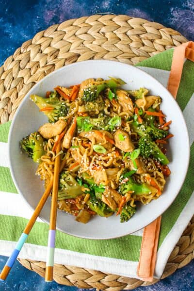 Healthy chicken and broccoli stir-fry with carrots, and noodles on a woven placemat.