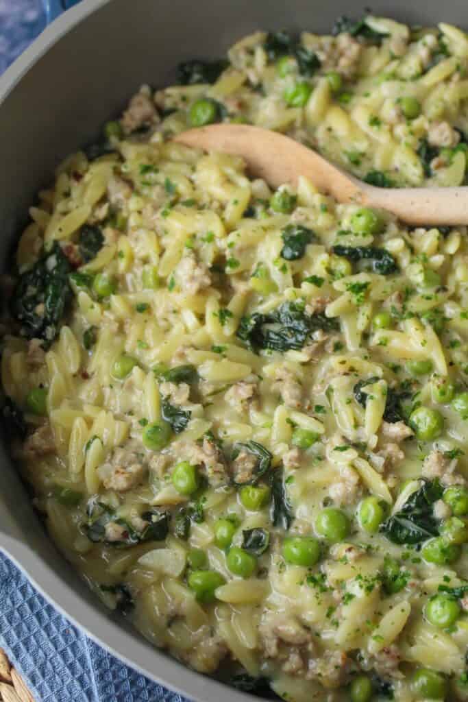 Creamy sausage orzo with peas and kale in a pan.