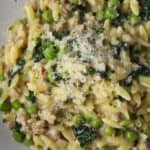 Creamy orzo with sausage, peas, spinach, and grated cheese in a bowl.