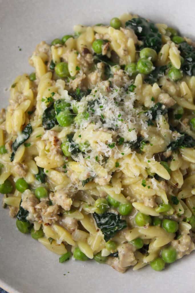 Creamy orzo with sausage, peas, spinach, and grated cheese in a bowl.