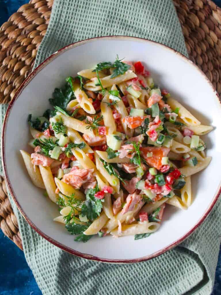 Pasta salad with salmon, cucumber, tomato and herbs in a white bowl.