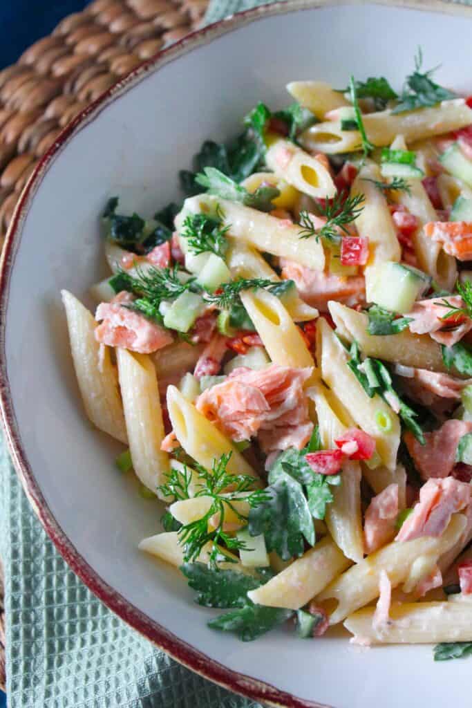 Colorful pasta salad with herbs, vegetables, and salmon in a white bowl.