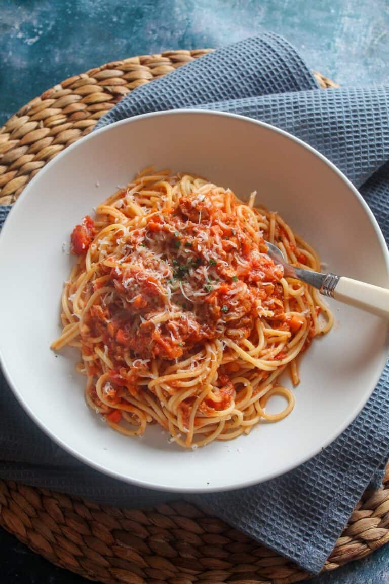 Spaghetti with tuna and tomato sauce served in a white bowl on a woven placemat.